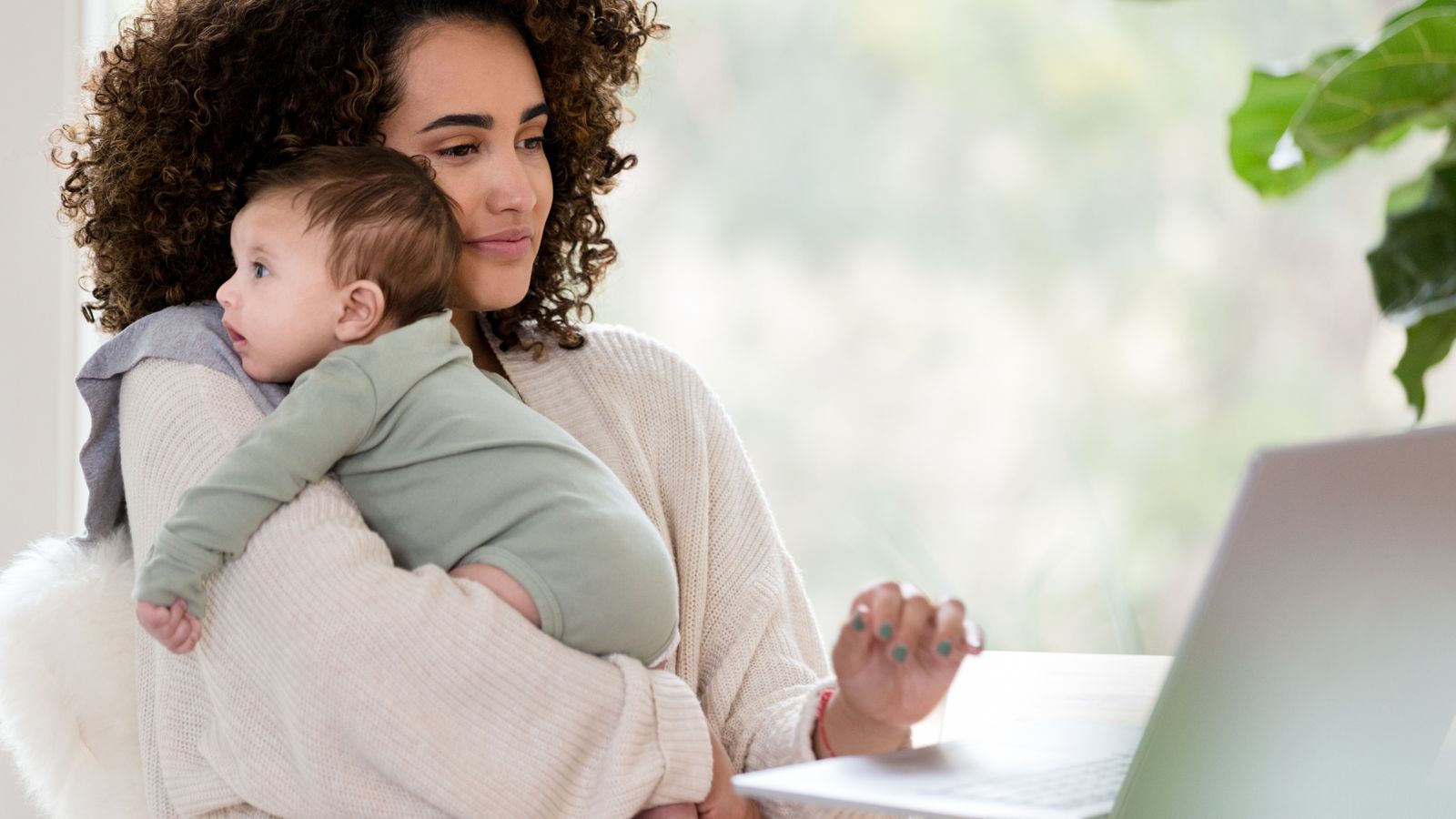 A mother at her laptop holding her baby close