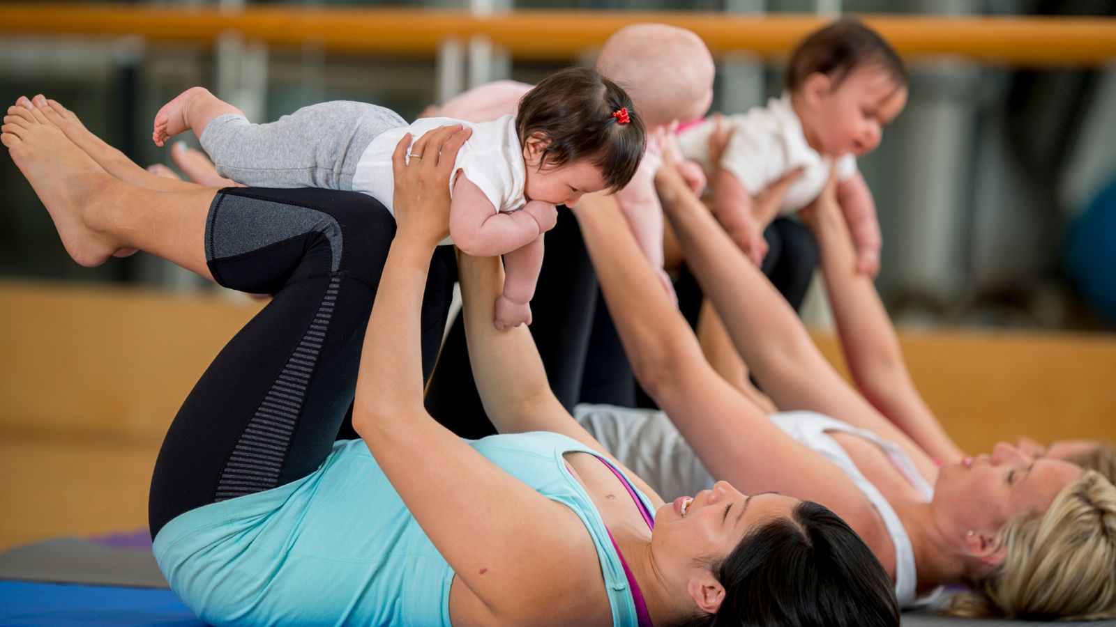 Moms in a baby yoga class lifting their little ones overhead