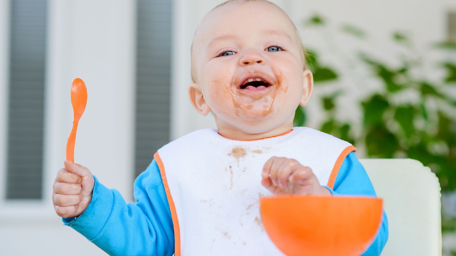 A laughing baby holding a little orange spoon