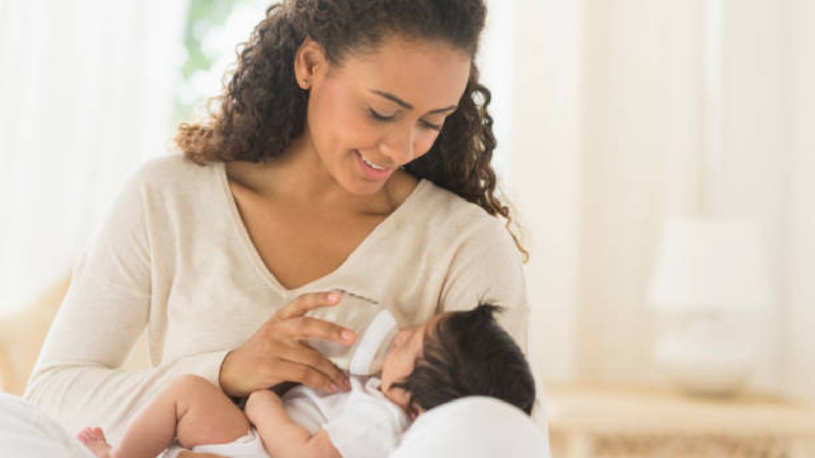 A smiling mother feeding her baby a bottle