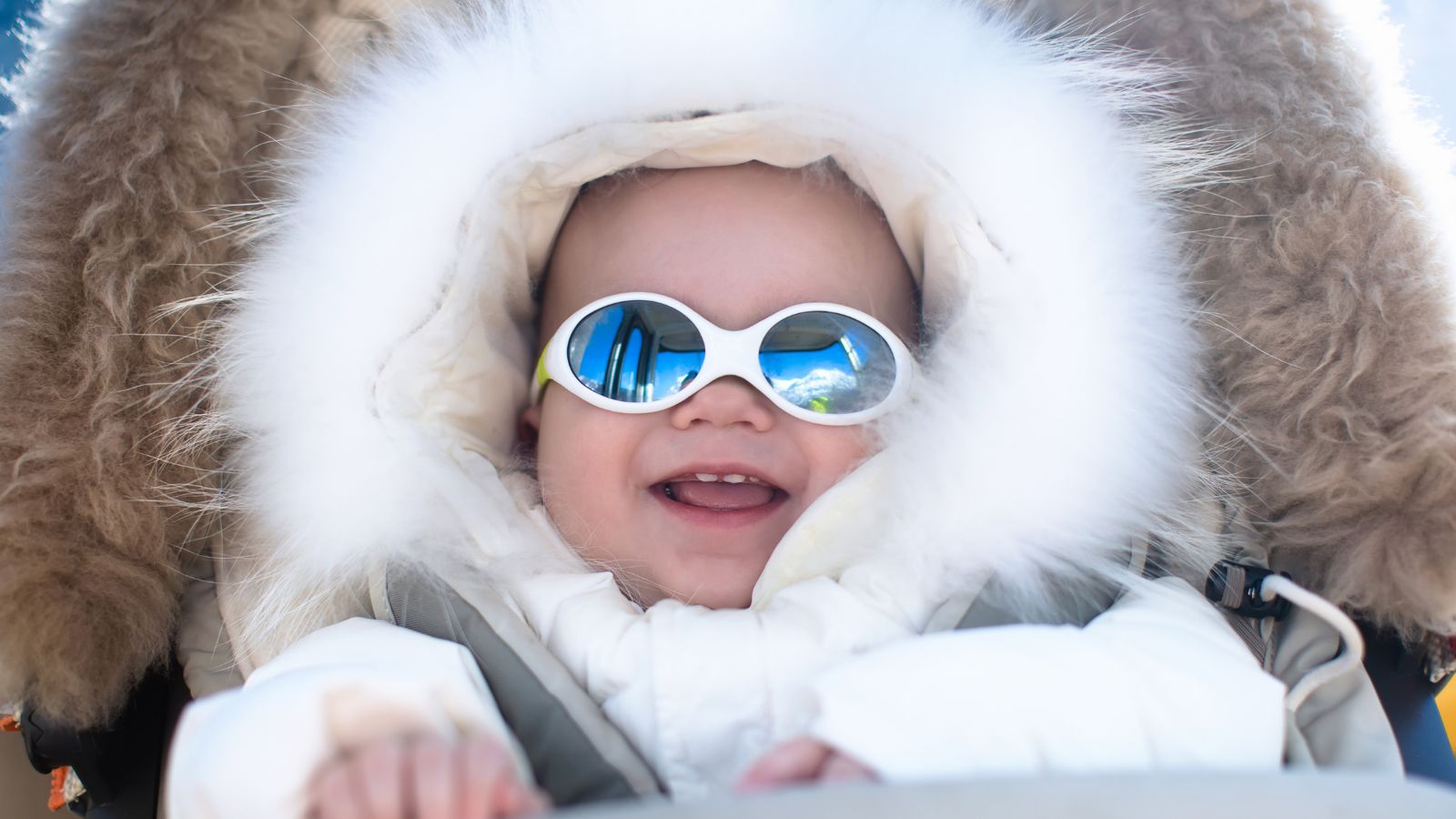 A laughing baby bundled in a fur-trimmed winter hood
