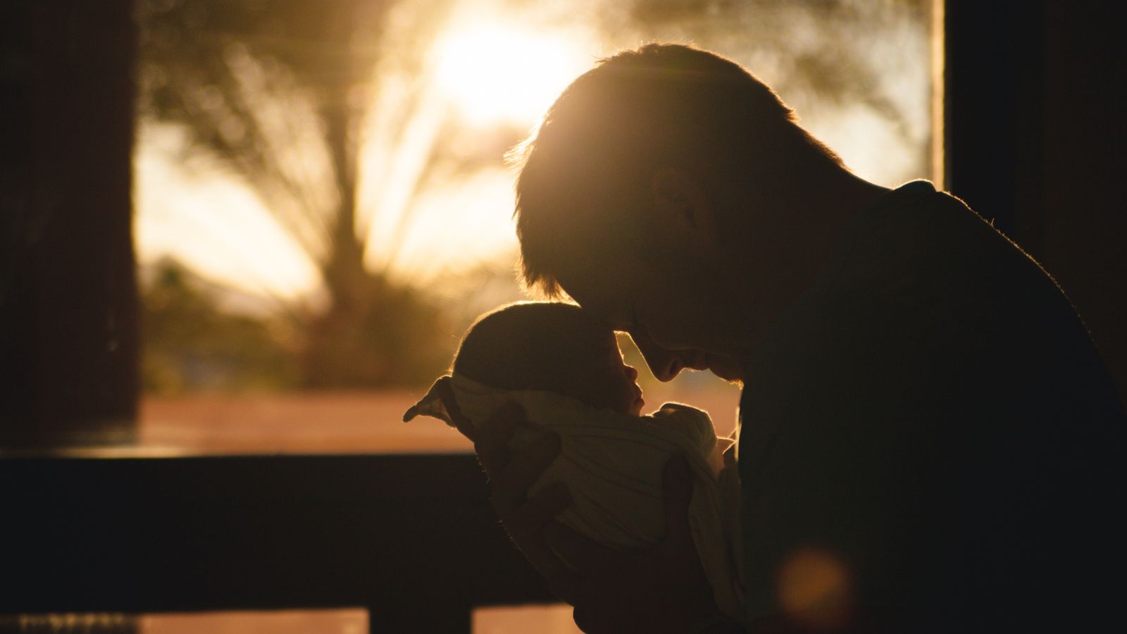 A father holding his newborn close in golden window light