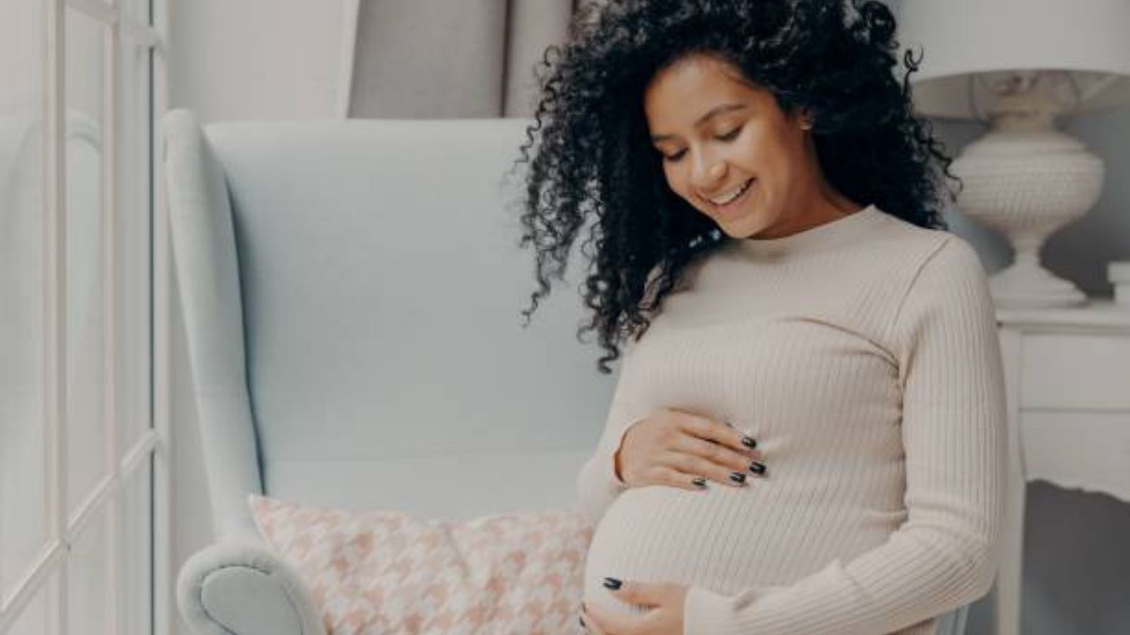 A smiling pregnant mother resting a hand on her bump in a bright nursery