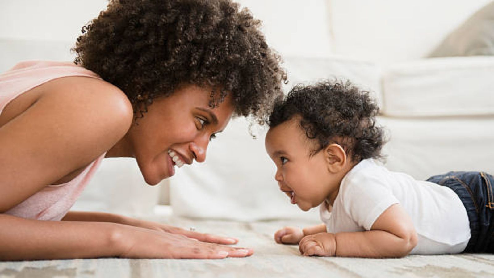 A mother lying on the floor, smiling nose to nose with her baby on his tummy