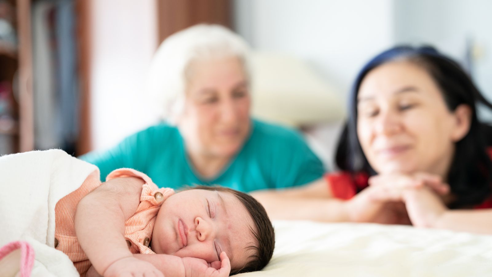 Grandma and mom smiling over a sleeping newborn