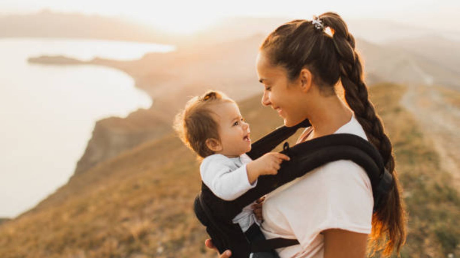 A mother carrying her baby in a front carrier on a sunlit hilltop