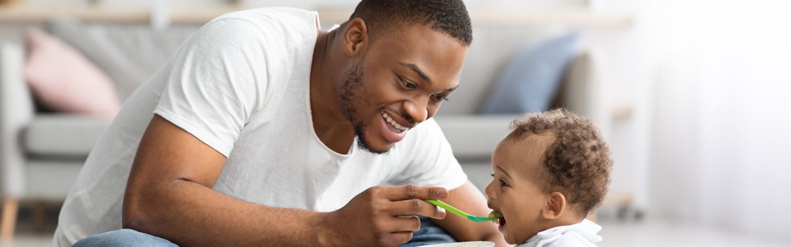 A father on the rug feeding his smiling baby