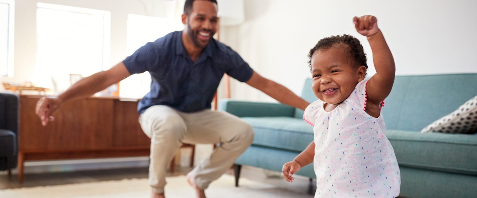 A father and his toddler daughter dancing in the living room