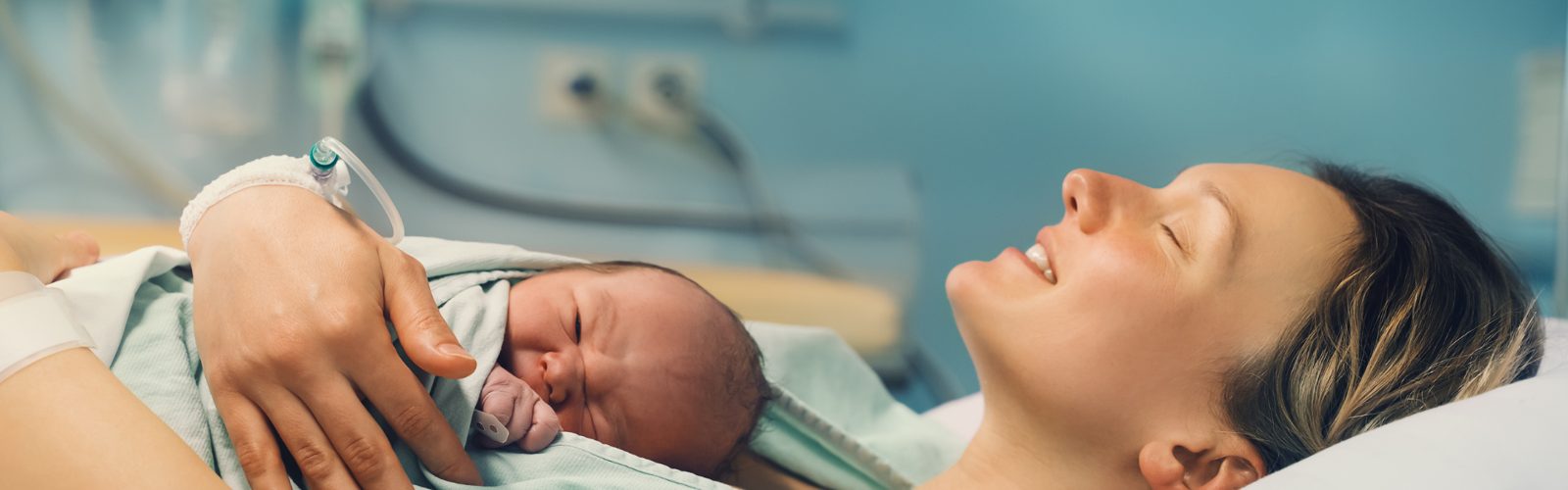 A new mother in a hospital bed, smiling with her eyes closed, her newborn on her chest