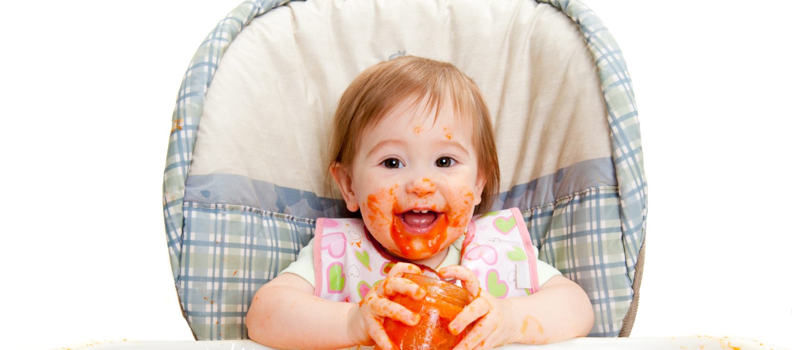 A baby covered in orange purée hugging the jar