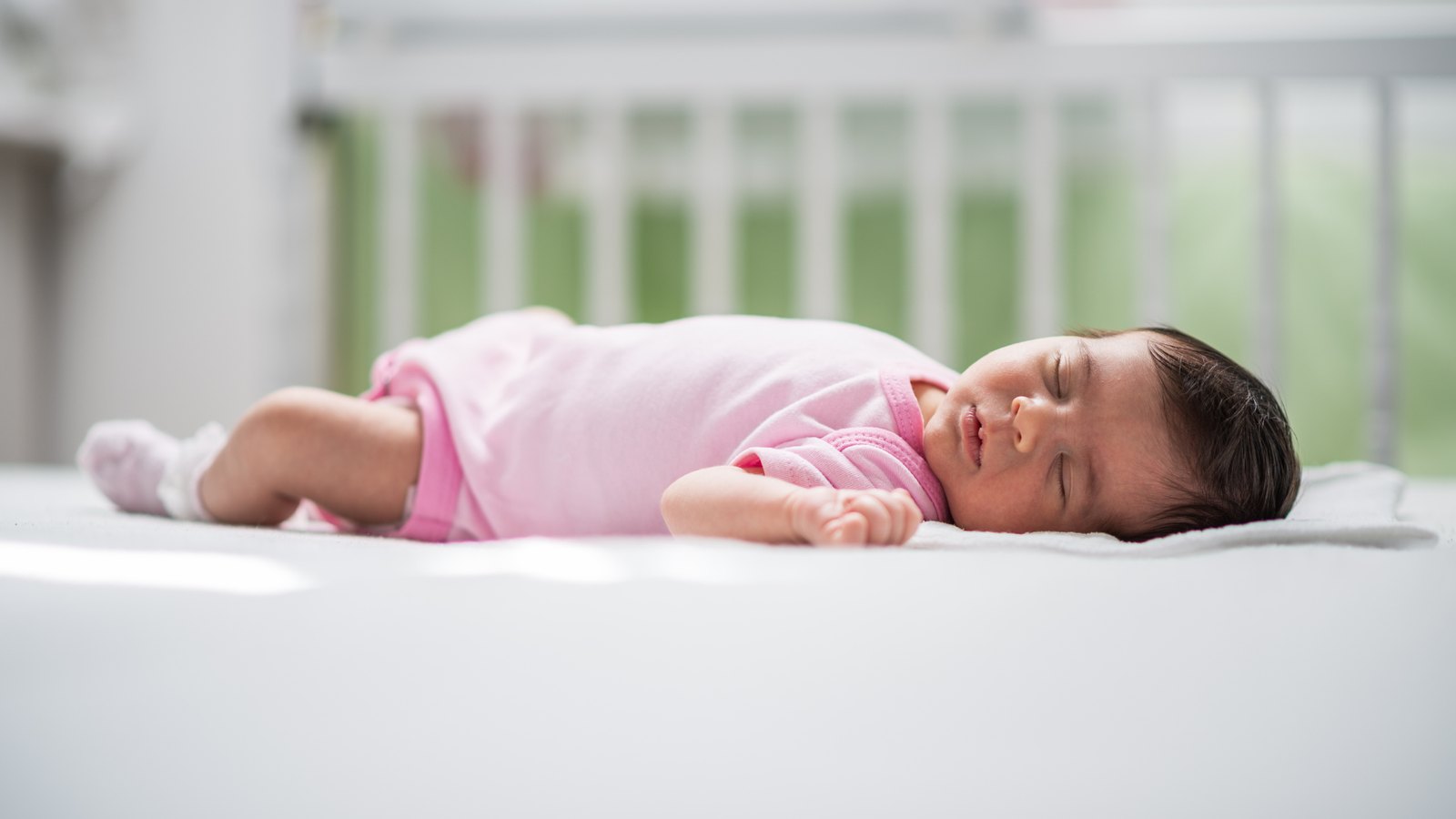 A newborn asleep on her back in her own crib, with nothing else in it